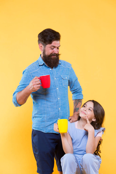 Water balance and health care. Family drinking tea. Bearded man and happy little girl holding mugs. Father and daughter drink tea at home. Tea party concept. Good morning. Having coffee together - Foto, afbeelding