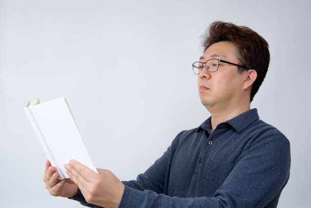 asiatischer Mann versucht, etwas in seinem Buch zu lesen. Sehschwäche, Presbyopie, Kurzsichtigkeit. - Foto, Bild