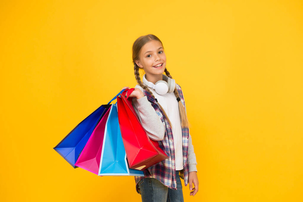 Dive into shopping. Happy child with paper bags. Little girl smile with shopping bags on yellow background. Holiday preparation and celebration. Shopping and sale on black friday. Addicted consumer - Photo, image
