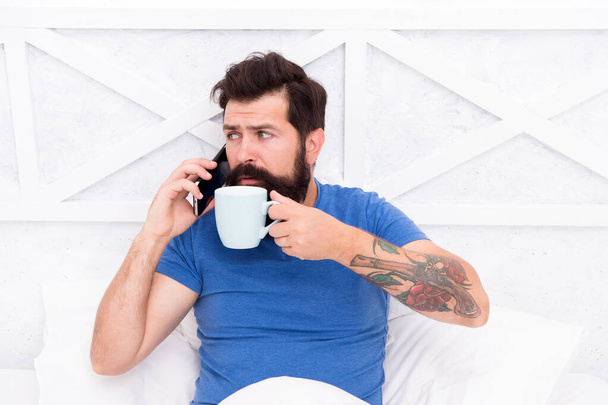 Pleasant conversation. Good morning. Modern life new technology. Technology concept. Hello dear. Bearded man using mobile technology in bed. Handsome guy talking on phone and drinking coffee at home - Foto, Imagem