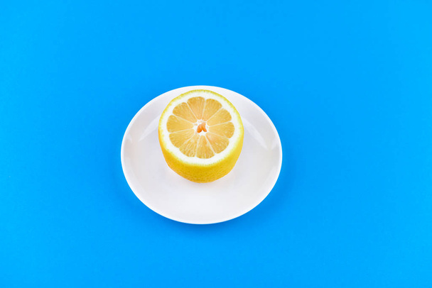 limão em um fundo azul. encontra-se em uma placa branca. meio limão cortado. vista de cima. lugar para gravar. Fatias de limão em um fundo azul. No verão, fatias frescas de laranja. Limão, fruta, refrescante, amarelado
 - Foto, Imagem