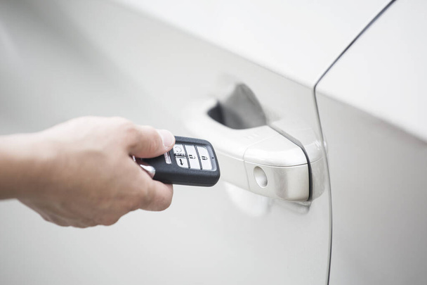 Menselijke hand die een sleutelloos apparaat of sleutelhanger vasthoudt om de nieuwe auto te openen en de auto te starten. focus op het sleutelloze apparaatsysteem en deurkruk - Foto, afbeelding