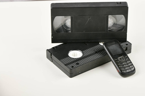 Retro-Objekte auf weißem Hintergrund. Druckknopftelefon und Videokassette. analoge Medientechnologie der Vergangenheit. Kopierraum - Foto, Bild