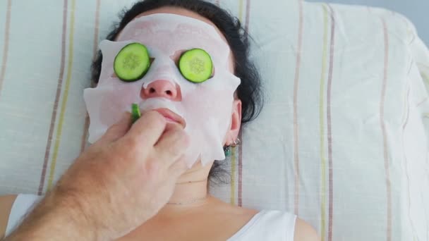 A male beautician makes a female client a vegetable therapy on her face in a spa salon. - Materiaali, video