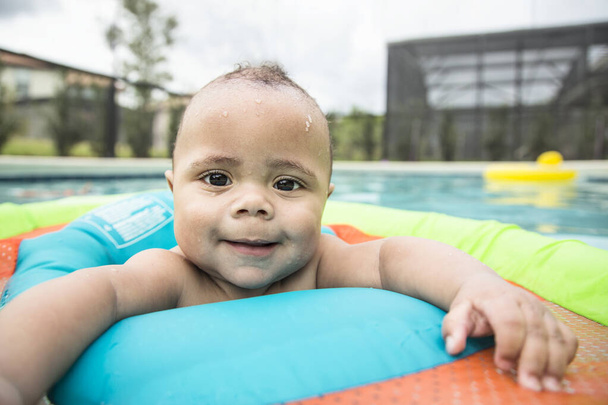 Sonriente niño biracial jugando en una piscina al aire libre. Un niño diverso que hace una expresión respetable - Foto, Imagen