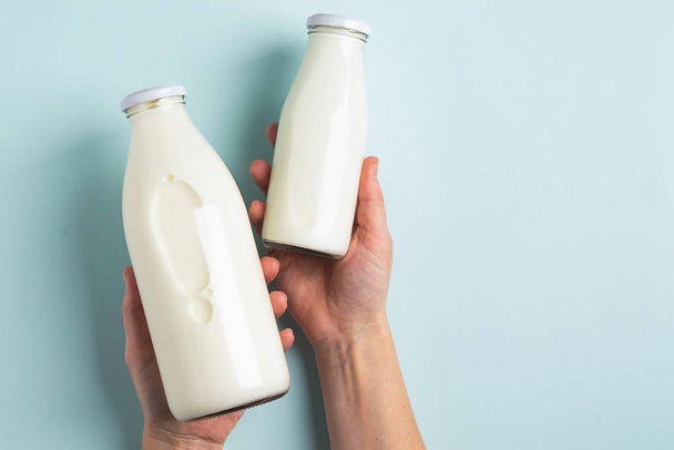 Vrouwelijke hand houdt twee flessen zure melk product blauwe pastel achtergrond. Het concept gezond dieet. Platte bovenaanzicht. - Foto, afbeelding