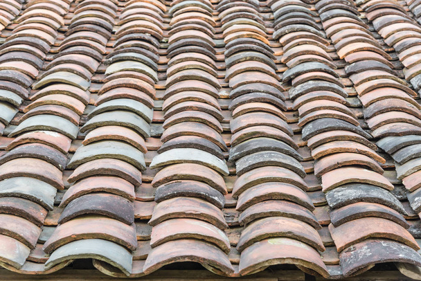 クローズアップビュー北ベトナムの古い家から様々な色で湾曲した粘土瓦の屋根、午後遅くの光。古代、風化した屋根瓦の表面、苔の質感。自然なシームレスなパターンの背景 - 写真・画像
