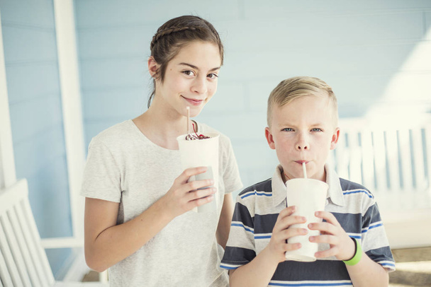 暖かい夏の日に屋外でミルクセーキや風味の飲み物を一緒に飲む2人のかわいい子供。冷たい液体のリフレッシュを楽しむ - 写真・画像