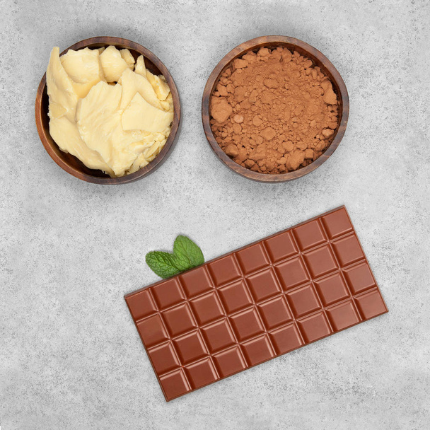 Bar of milk chocolate, cocoa powder, cocoa butter and mint on gray stone background - Foto, Bild