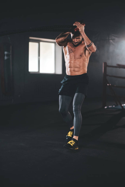 Σε μια σύγχρονη cross fitness τάξη bodybuilding άνθρωπος κάνει ασκήσεις με τα σχοινιά συγκεντρωμένα εργάζεται σκληρά μπροστά από την κάμερα - Φωτογραφία, εικόνα