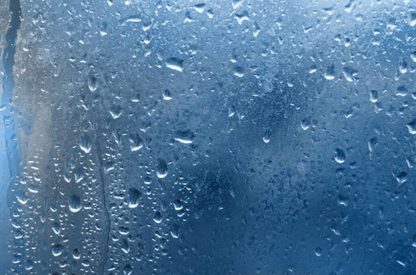 Дощ падає на віконне скло. фон з синіх дерев 2020 року
. - Фото, зображення