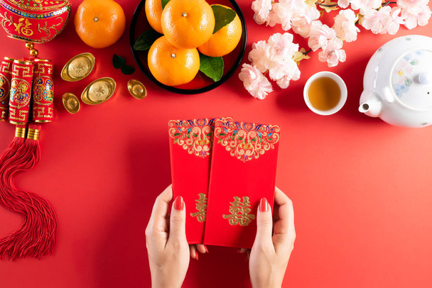 Chinese new year festival decorations. Woman hand holding pow or red packet, orange and gold ingots on a red background. Chinese characters FU means fortune good luck, wealth, money flow. - Photo, image
