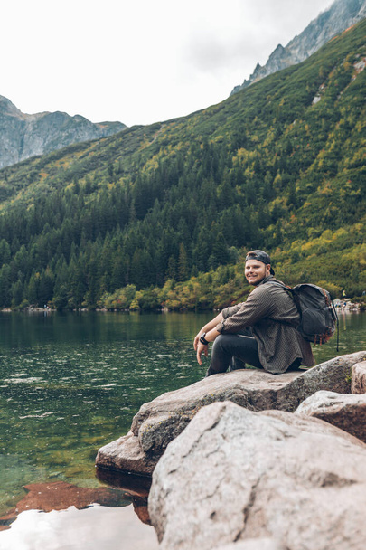 man sitting on the rock in front of lake in mountains enjoying the view - Fotoğraf, Görsel