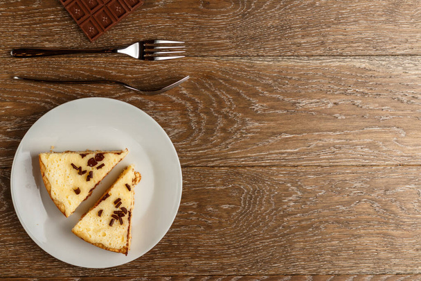 Homemade cheesecake sprinkled with chocolate chips on a white plate. Wooden background, top view and copy space - Φωτογραφία, εικόνα