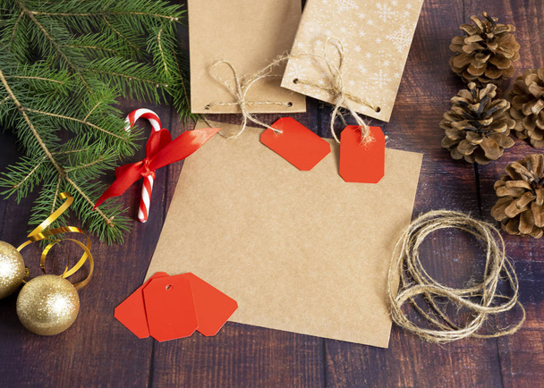 Gift bag made of handmade kraft paper on a wooden background in a Christmas style, decorated with Christmas tree balls, cones, a ball of rope, fir branches. Christmas, New Year, winter holiday. - 写真・画像