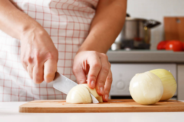 Woman cooking at home in the kitchen, cutting onions on a wooden board. Healthy fresh food. Close-up - Photo, image