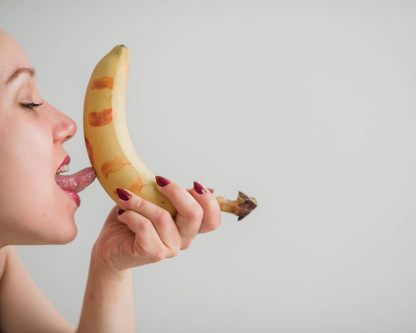 Close-up of the face, lips, tongue of a young, European girl licking a big yellow, sweet banana. - Фото, зображення