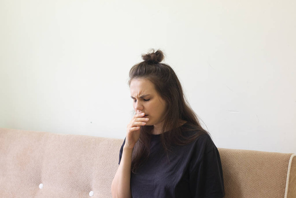 Mujer joven enferma se sienta en casa con dolor de garganta y tos
. - Foto, imagen