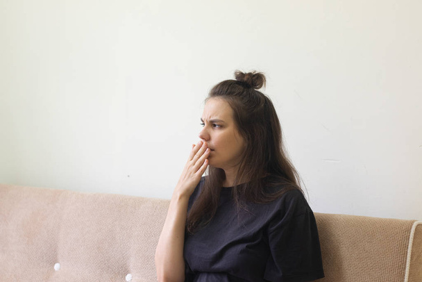Sick young woman sits at home with a sore throat and coughs. - 写真・画像