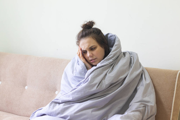 Хвора молода жінка в ковдрі сидить вдома з сильним головним болем
. - Фото, зображення