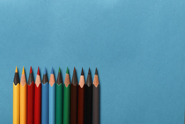 Multicolored pencils lie on blue paper background - Fotoğraf, Görsel