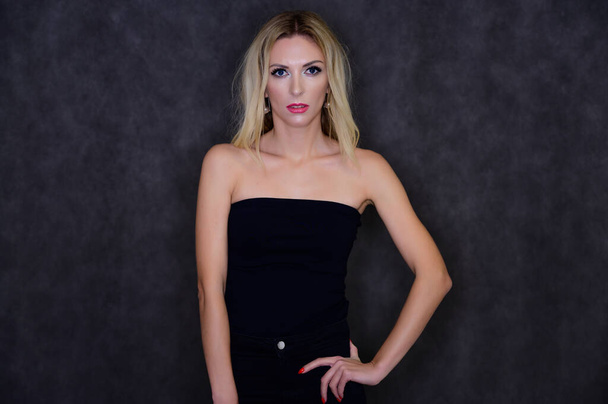 Artistic portrait of a pretty slim blonde model with excellent makeup and beautiful hair in a black top on a gray background. Stylish, fashionable, youth, sexy. This is in different poses. - Фото, зображення
