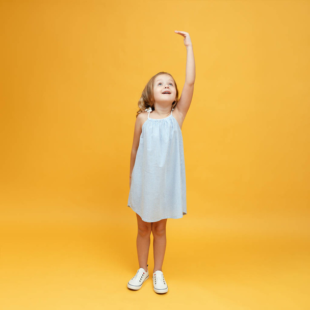 A little child measures her height on a yellow background. Concept of development, goal, success - Photo, Image