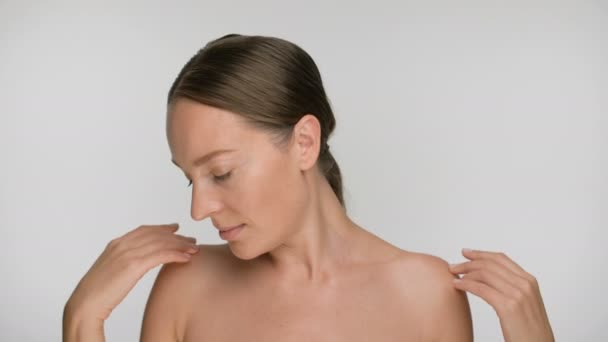 Close-up beauty portrait of young woman with smooth healthy skin, she gently touches her neck and shoulders with her fingers on white background - Imágenes, Vídeo