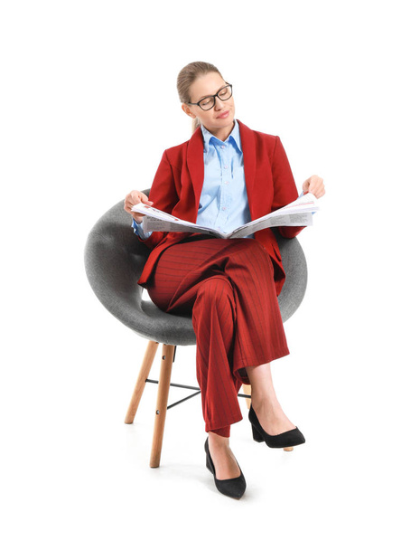 Young businesswoman with newspaper sitting in armchair against white background - Photo, image