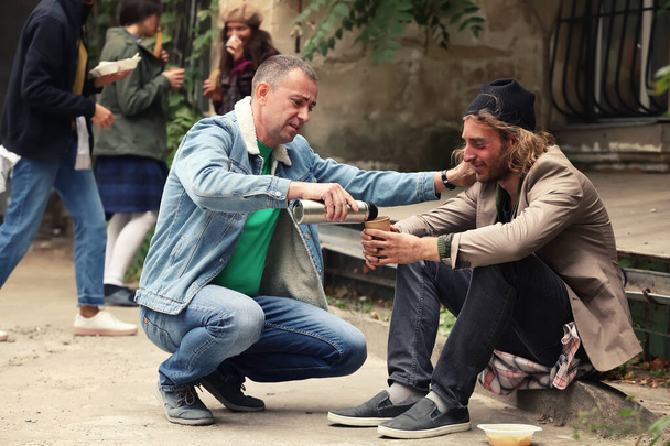 Доброволець дає напій безпритульному на відкритому повітрі
 - Фото, зображення