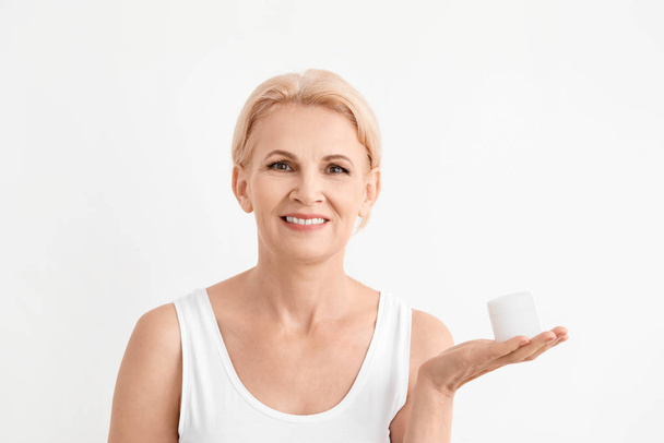 Mature woman with jar of cream on white background - Foto, Imagen