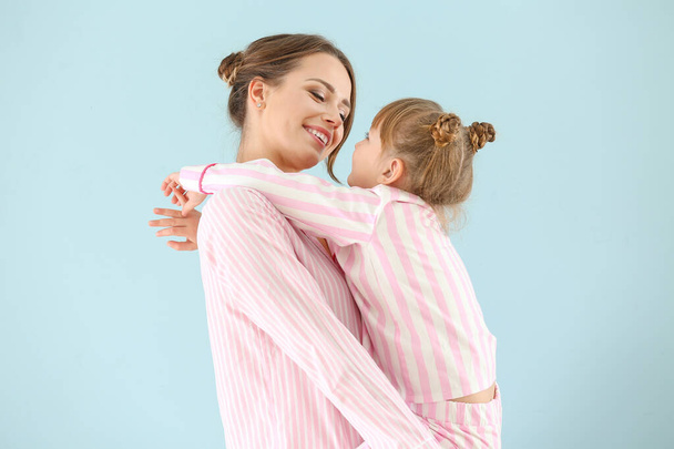 Portrait of happy mother and daughter in pajamas on color background - Foto, afbeelding