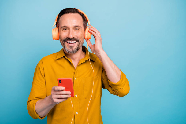 Ritratto di uomo allegro hanno pausa ascoltare musica dal suo smartphone utilizzando moderno auricolare arancione abbigliamento stile di vita vestito isolato su sfondo di colore blu
 - Foto, immagini
