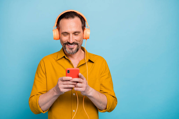 Portrait of positive cheerful man use cellphone listen online sound track he search on internet have modern headset wear stylish clothing isolated over blue color background - Foto, Bild