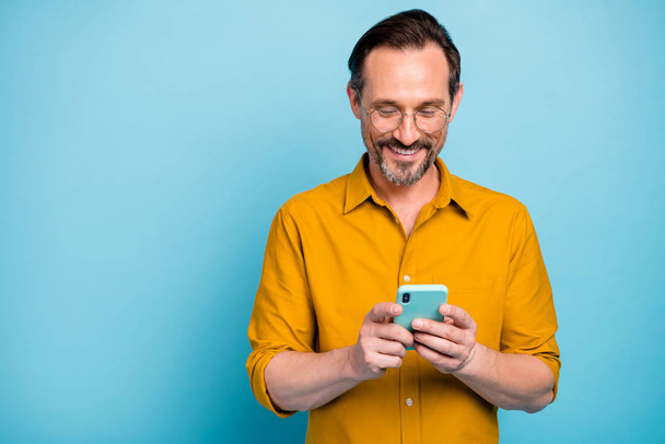 Portrait of cheerful attractive mature man modern device user use his smart phone type social network message wear good looking clothes isolated over blue color background - Фото, изображение