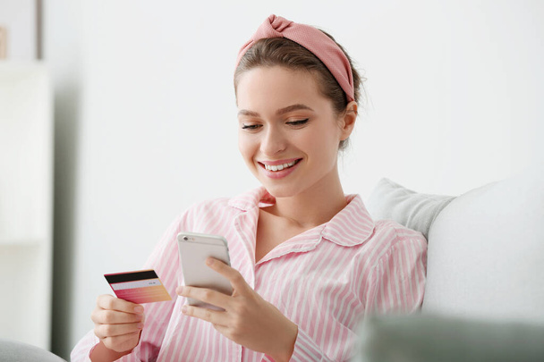 Jeune femme avec carte de crédit et téléphone mobile shopping en ligne à la maison
 - Photo, image