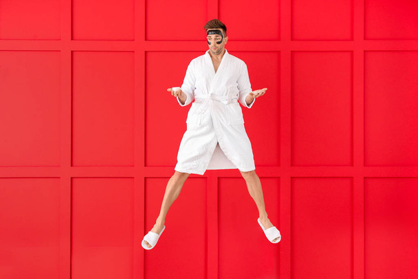 Jumping young man in bathrobe and with coffee on color background - Fotoğraf, Görsel