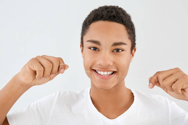 Portret van tiener jongen met tandzijde op lichte achtergrond - Foto, afbeelding