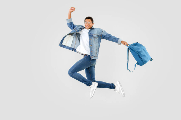 Salto adolescente afroamericano con mochila sobre fondo blanco
 - Foto, imagen