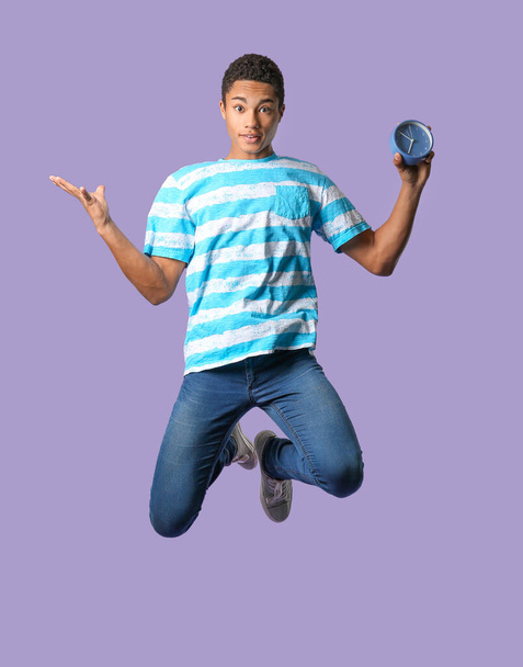 Jumping African-American teenager boy with clock on color background - Foto, Imagen