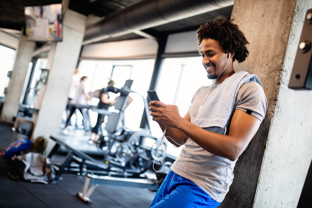 Giovane uomo muscoloso che utilizza il telefono cellulare in palestra in pausa allenamento - Foto, immagini
