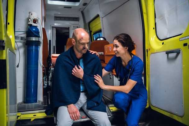 Woman in medical uniform talks friendly and smiles to a man in blanket - Photo, Image