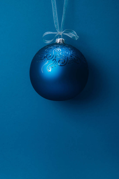 Christmas ball hanging on a ribbon over blue background. Copy space. - Фото, изображение