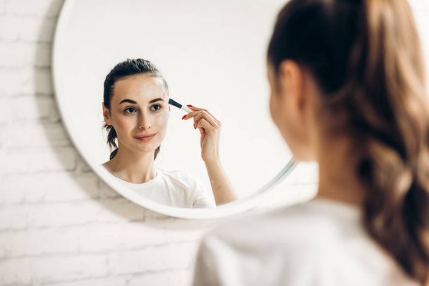 Beautiful young woman applying makeup in bathroom. - Foto, afbeelding