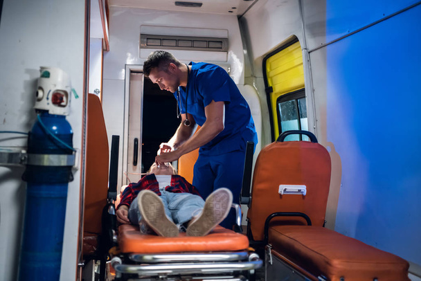 Lijkschouwer zet een masker op zinloze vrouw liggend op brancard in de ambulance auto - Foto, afbeelding