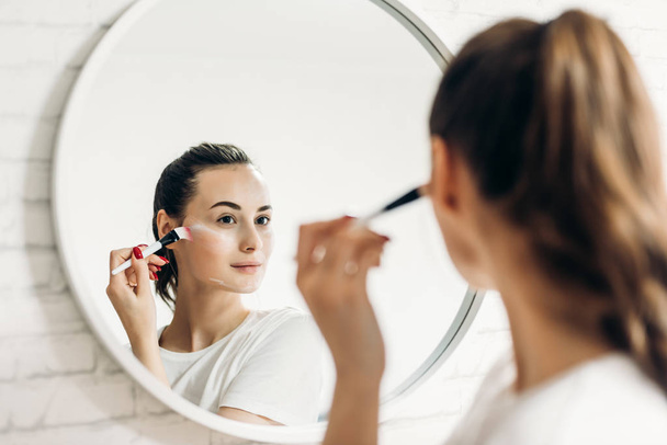 Beautiful female applying cosmetics on her face. - Valokuva, kuva
