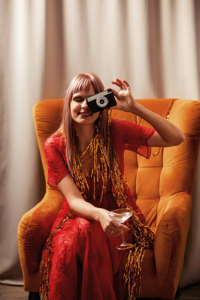 Стильная женщина в платье сидит в классическом кресле с винтажной камерой
 - Фото, изображение