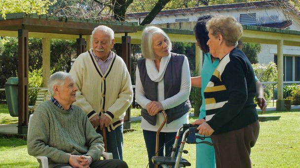 アフリカの看護師は、リハビリ病院の庭の屋外で2人の高齢者の退職したカップルと話します。幸福とリハビリテーションと退職の概念. - 写真・画像