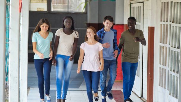 Πολυεθνική ομάδα μαθητών που περπατούν στο διάδρομο του σχολείου. Ευτυχία και ελαφρότητα. - Φωτογραφία, εικόνα
