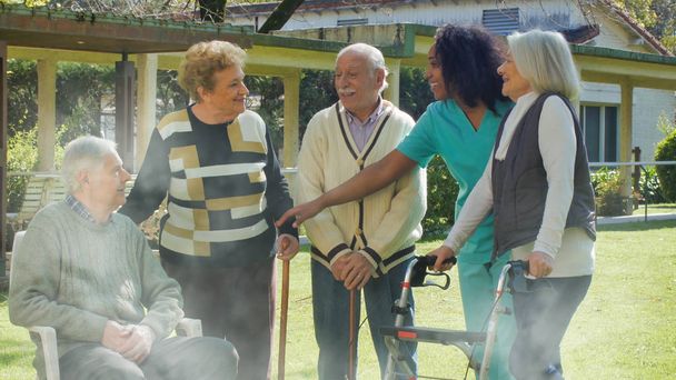 アフリカの看護師は、リハビリ病院の庭の屋外で2人の高齢者の退職したカップルと話します。幸福とリハビリテーションと退職の概念. - 写真・画像